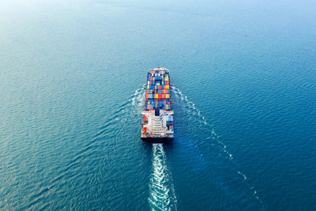 Operação logística de importação com navio cargueiro repleto de contêineres coloridos navegando em mar azul sob luz natural