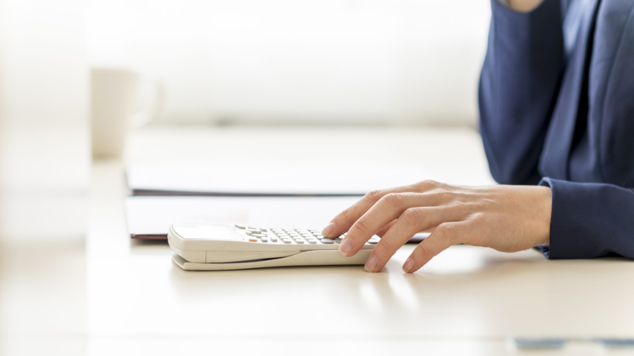 Close up shot of female bookkeeper hand calculating annual expenses and incomes on white calculator.